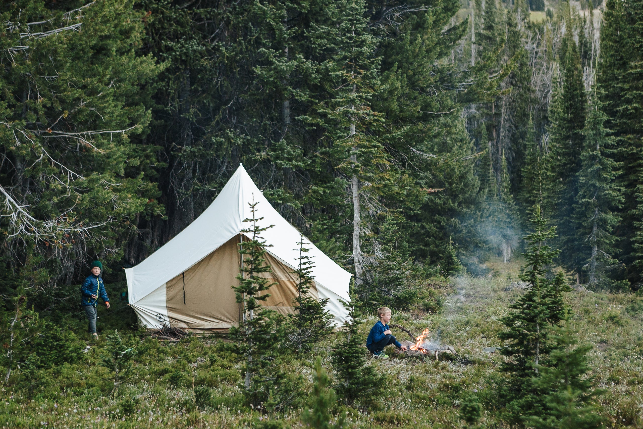Two people camping in a forest with a white tent.